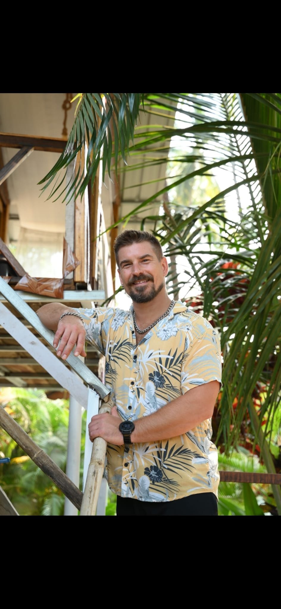 Coach Phill Terp in a tropical garden setting, leaning on a wooden staircase surrounded by palm fronds